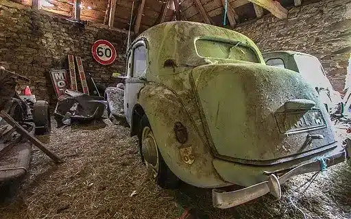 Vieille voiture dans une grange, signalisation 60. Abandonnée, poussiéreuse.
